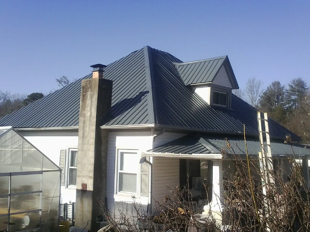 Dark blue standing seam metal roof on a white farmhouse with dormer — Slate & Tile Roof Repair by Roofing Brothers in Amberson