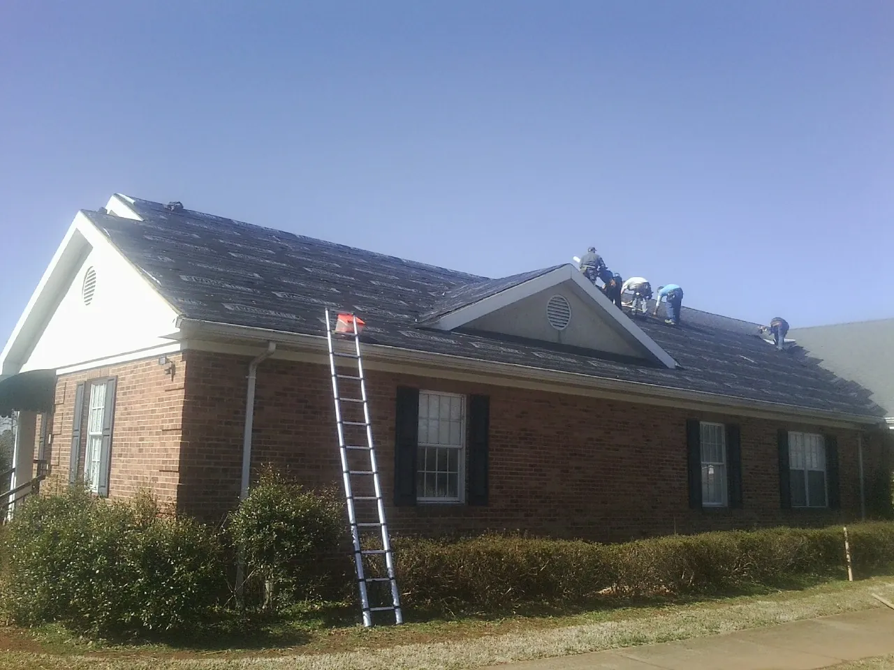 Crew tearing shingles off a brick ranch roof with a ladder set — Emergency Roof Repair work by our crew in Amberson