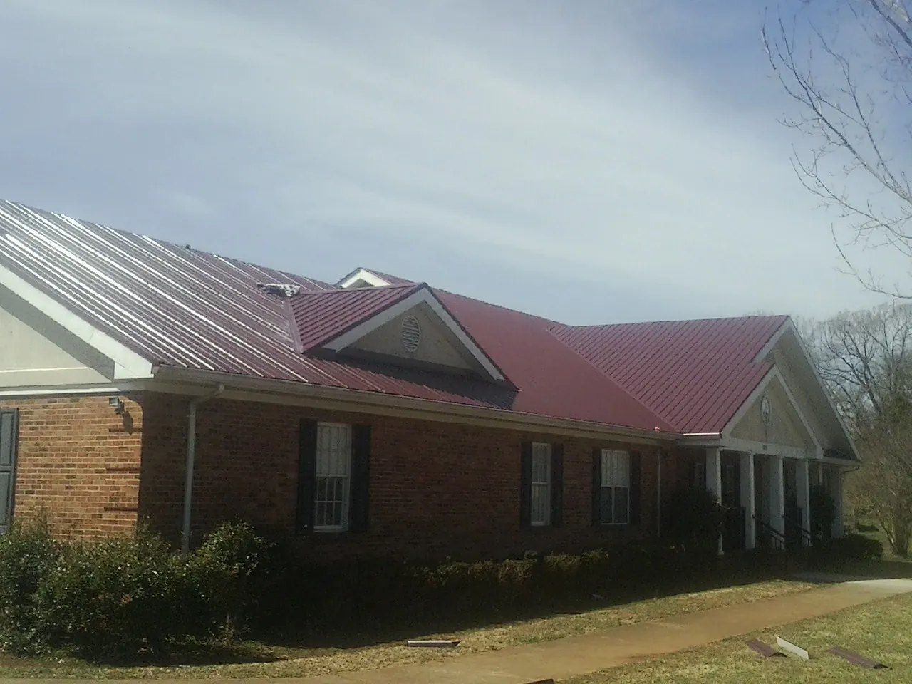 Red metal roof with gabled entries on a long brick building, from a Hail Damage Roof Repair job in Amberson