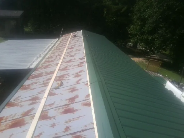 Old rusted panels beside newly installed green metal roofing — Wind Damage Roof Repair by Roofing Brothers in Amberson