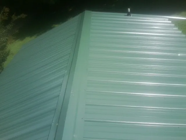 New green metal panels meeting at the ridge of a roof — Flat Roof Repair work by our crew in Amberson