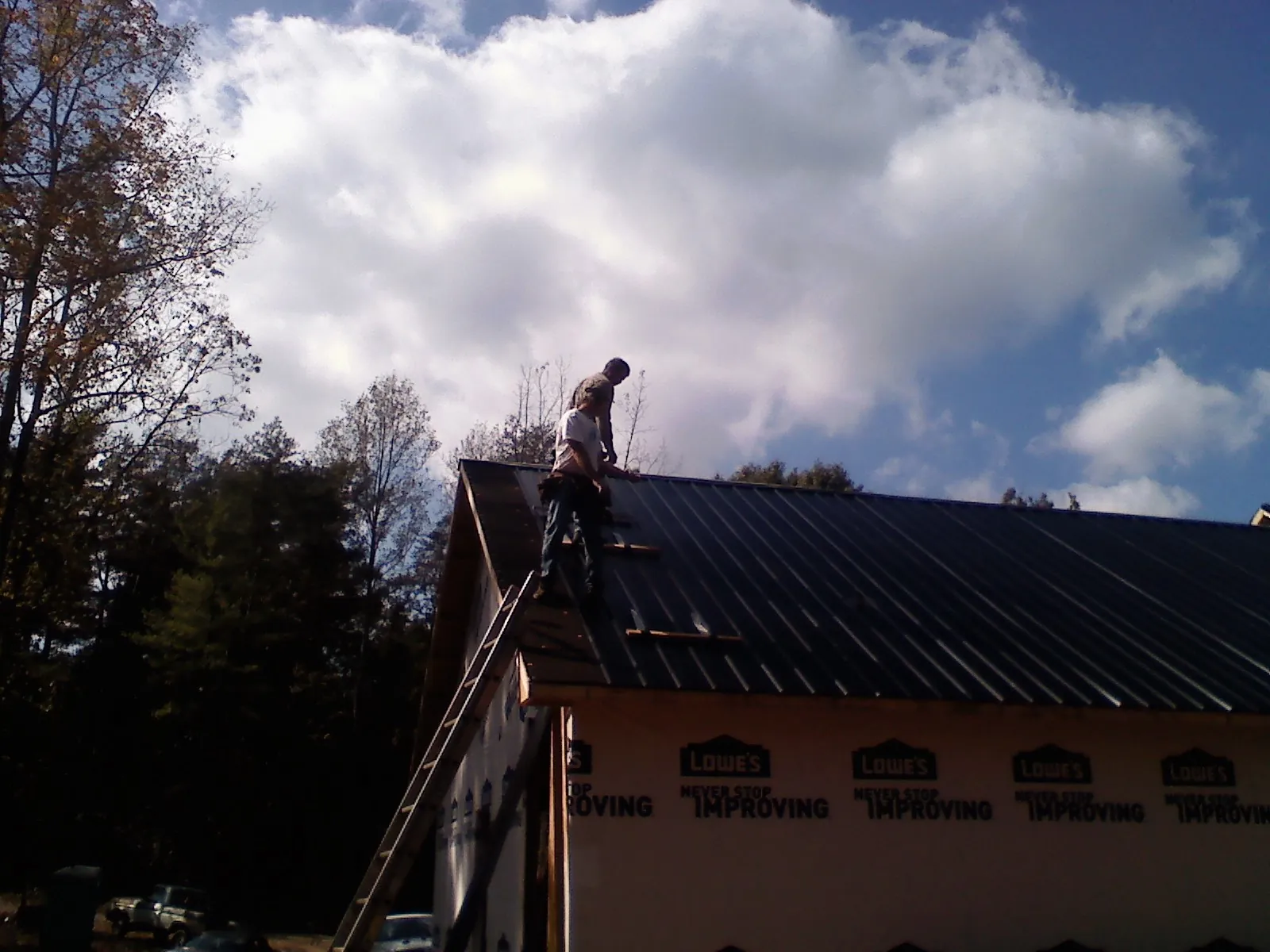 Roofer fastening dark metal panels high against a cloudy sky, from a Roof Inspection job in Amberson