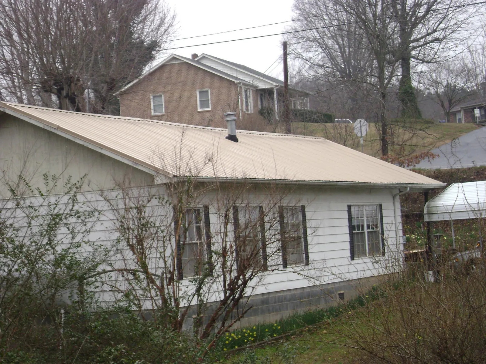 Tan metal roof on a white sided house set into a hillside — Commercial Roofing by Roofing Brothers in Amberson
