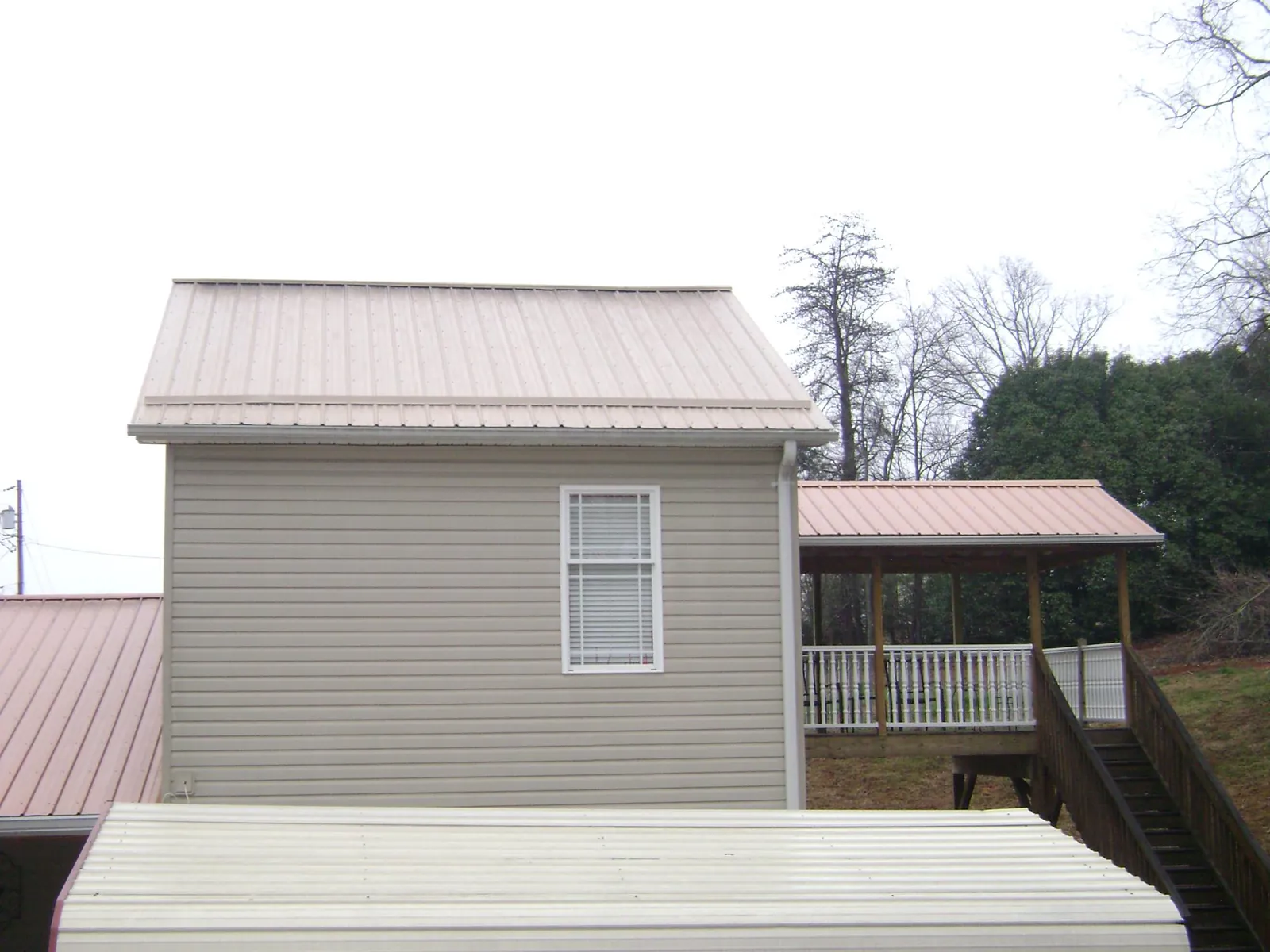 Tan metal roofs on a two story addition and attached porch, from a Roof Replacement job in Amberson
